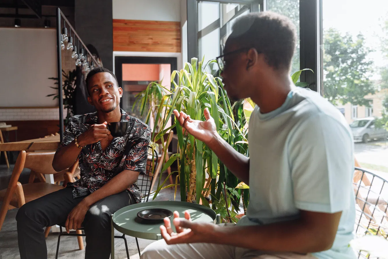 Two people in an easy, animated conversation over coffee in a plant-filled cafe